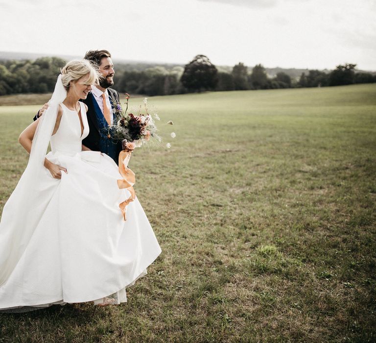 Bride in a Jesus Peiro wedding dress walking across a field with her groom 