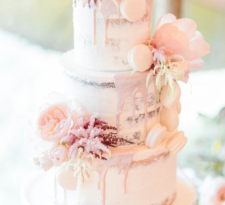 Three tier semi-naked cake with pink drip icing, decorated with pink flowers and macarons