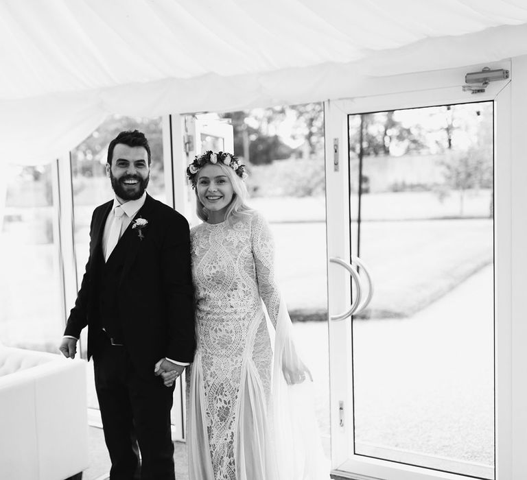 Bride in Grace Loves Lace wedding dress and single tier cathedral length veil stands in marquee entrance with groom in black Hugo Boss suit at Drenagh Estate Wedding