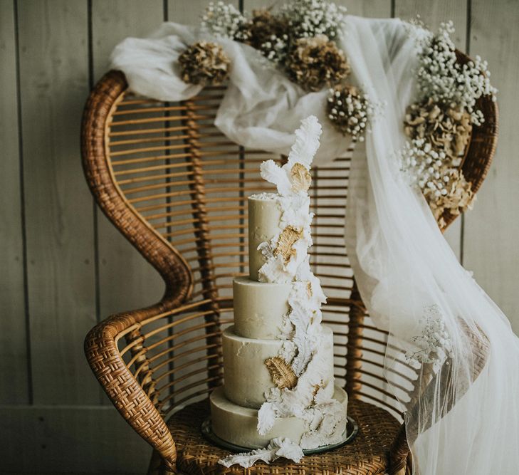 Four tier buttercream wedding cake with feather design resting on a peacock chair 