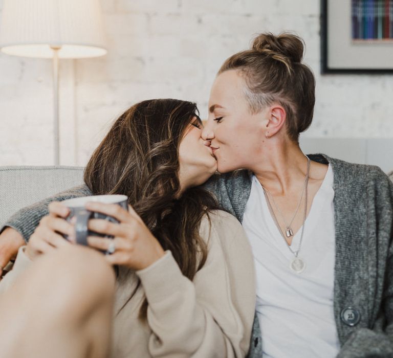 The brides share a happy kiss on the sofa before their elopement