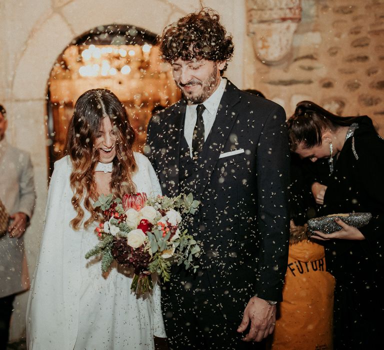 The bride and groom leaving their church wedding ceremony having confetti thrown over them