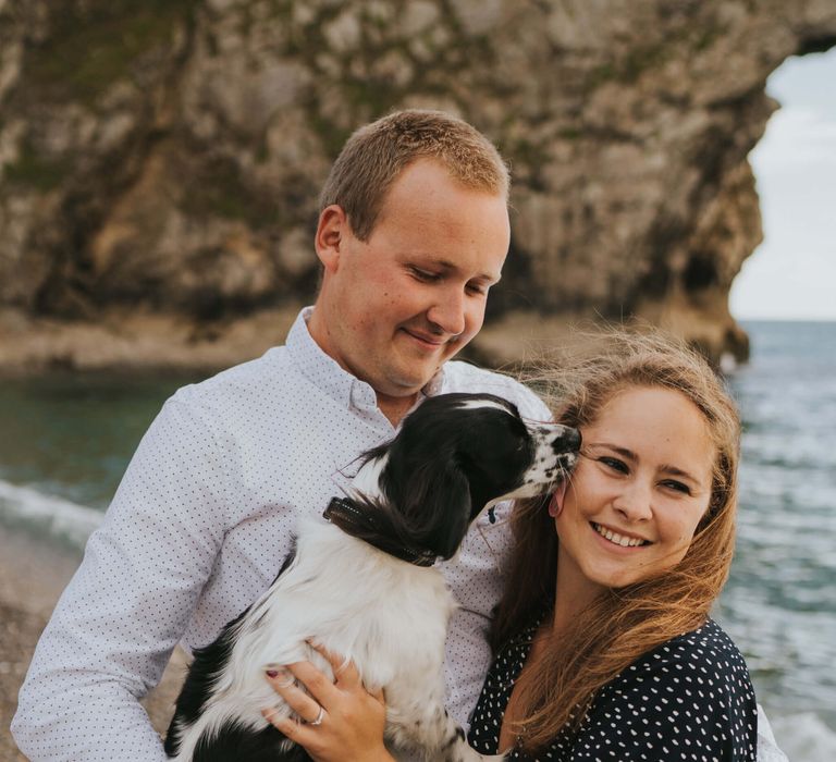 Newly engaged couple holding each other and their dog at the beach