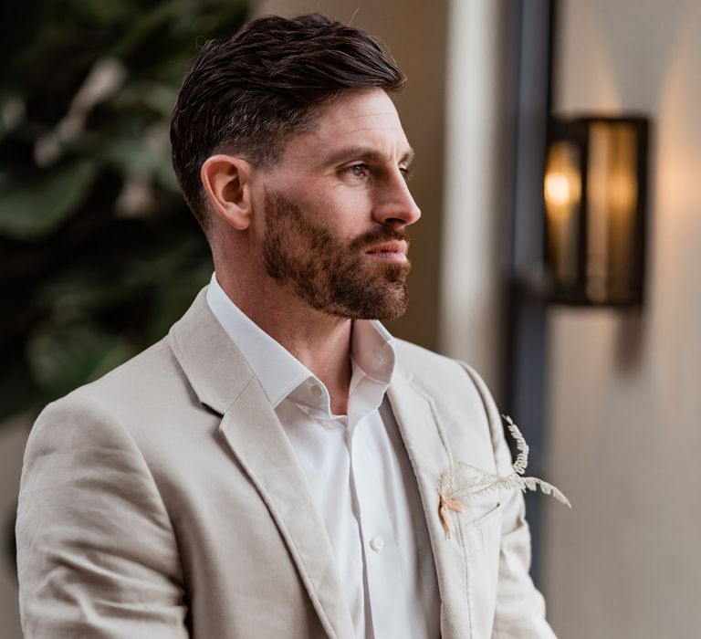 Groom in a light beige wedding suit with dried grass buttonhole 