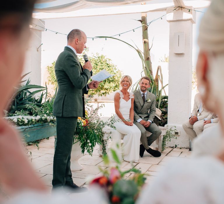 Wedding celebrant reading aloud at the wedding ceremony as the bride and groom look on