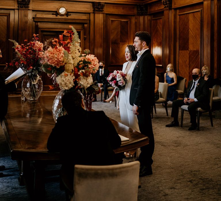 Bride & groom stand at the front as they say their vows with wedding party surrounding them