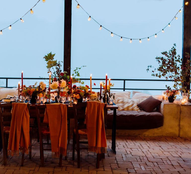 Intimate wedding dinner in the Italian mountains with yellow scarves over guest chairs and red and orange floral centrepieces