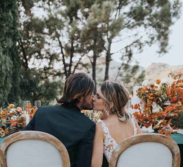 Bride and groom share a kiss as they eat dinner at intimate elopement