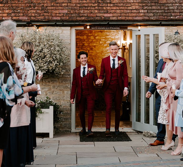 A gay couple leave their wedding ceremony. They both wear burgundy suits and are smiling. Photography by Cat Stephens. 