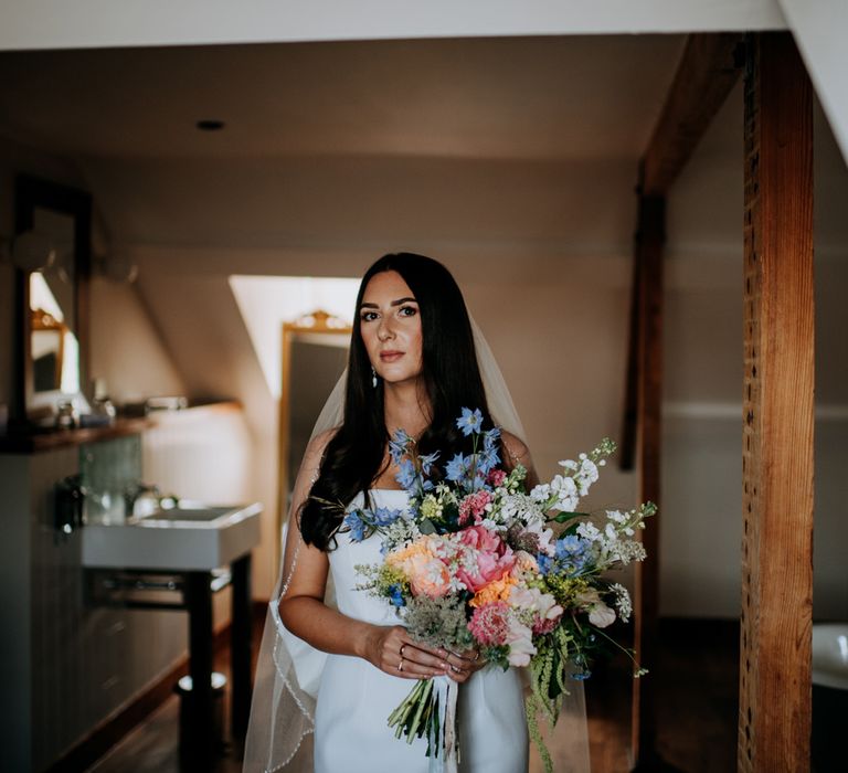 Bride with long brown hair wearing white strapless Rebecca Vallance Dress holds multicoloured bridal bouquet in the Hotel du Vin Harrogate before wedding