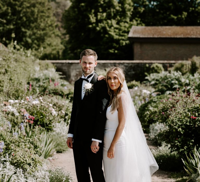 Bride & groom stand within West Dean Gardens 