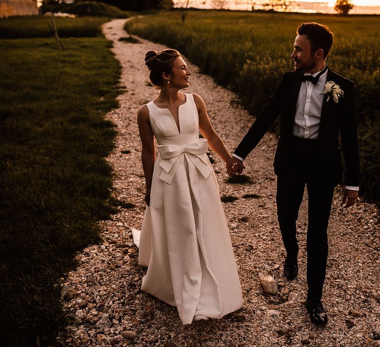 Bride & groom walk hand in hand as bride wears textured wedding gown