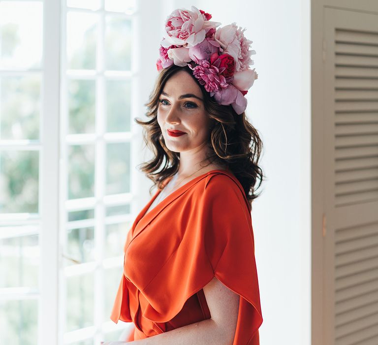 Bride wears red gown with pink bridal crown as she stand beside window on her wedding day in Menorca