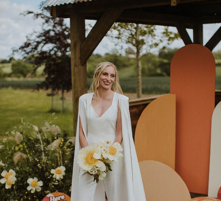 Stylish bride in a jumpsuit with cape and red velvet platform shoes 