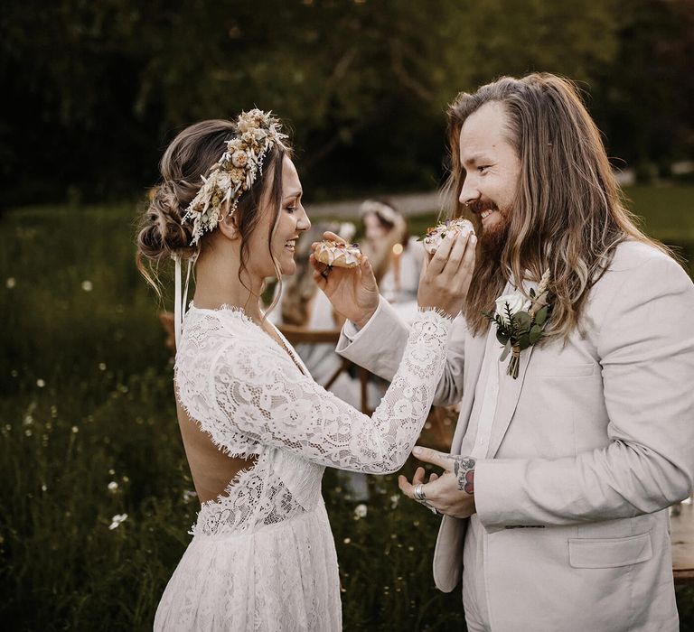 Bride in a lace long sleeve wedding dress feeding her groom a doughnut in a beige wedding suit 