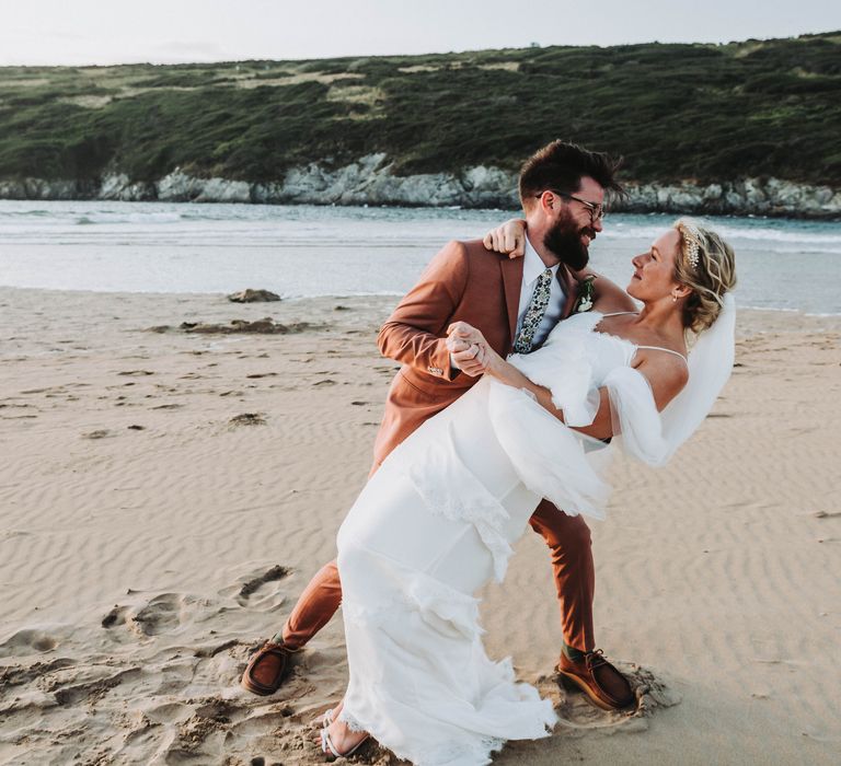 Groom leans his bride back on the beach in Cornwall on their wedding day