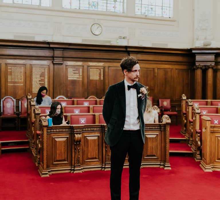 Groom waits for his bride at the altar in Town Hall whilst wearing deep green velvet suit