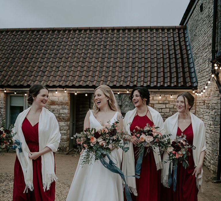 Winter wedding with bridesmaids in different floor-length burgundy dresses wearing white shawls 