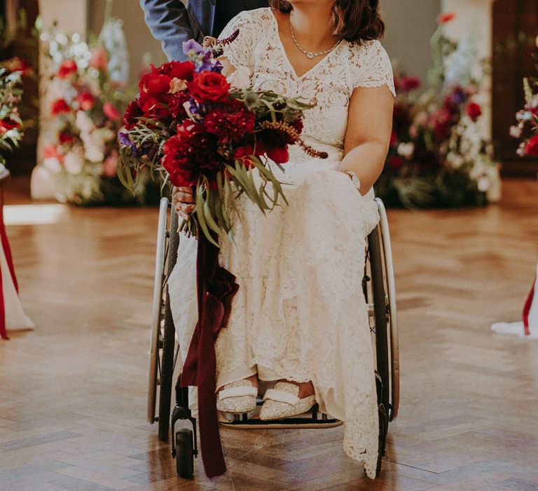 Bride and groom wedding ceremony descent with groom in a blue suit pushing his bride in a wheelchair up the aisle 