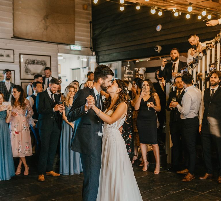 Bride & groom kiss during first dance as wedding guests watch and take photos