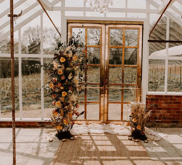 Brass door in the glasshouse at The Gooseberry House with vertical flower arrangements decorating the entrance 