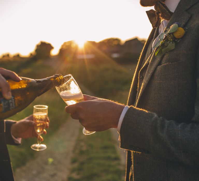 Grooms cheers outdoors and pour wine as the sun sets behind them | Story + Colour