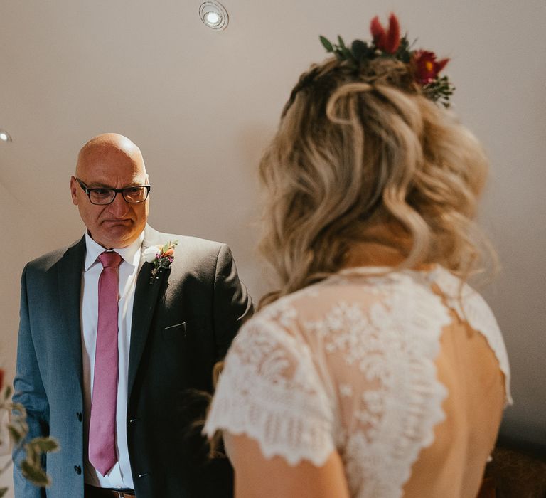 Father of the bride in dark suit and pink tie looks at bride in open back lace cap sleeved wedding dress before late summer wedding in Norfolk