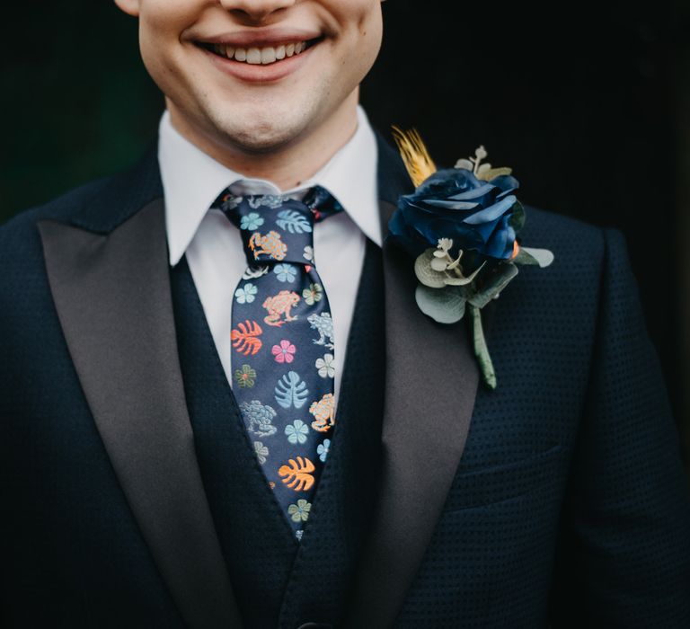 Smiling groom in dark blue suit, white shirt, blue florals tie and blue rose buttonhole for The Wellbeing Farm wedding 