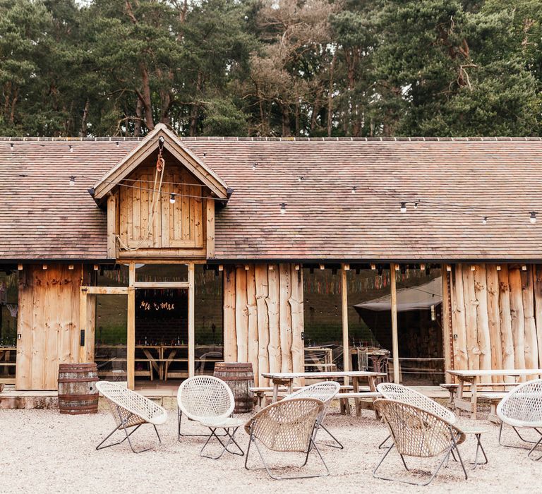 Wooden clad exterior of The Bridal Barn in Claverley for summer wedding with fairy lights and rattan garden chairs