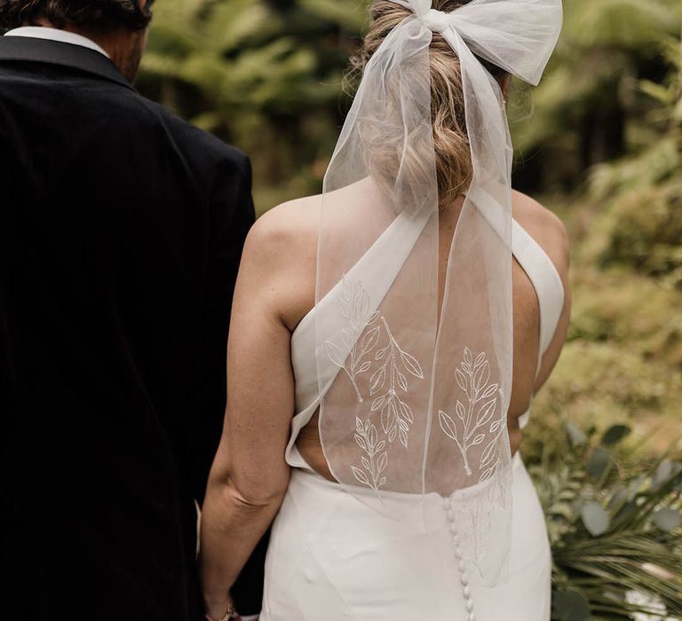 Bride in an embroidered bow wedding hair accessory and halterneck wedding dress with low back detail and buttons