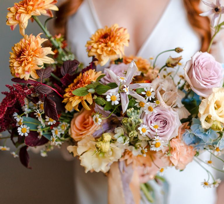 Bride holding multicoloured bouquet with purple roses, daises and pastel florals 