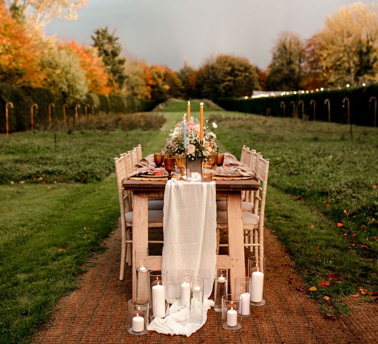 Rustic outdoor wedding reception with wooden tables and chairs, candles, pastel florals and amber glassware in orchard 