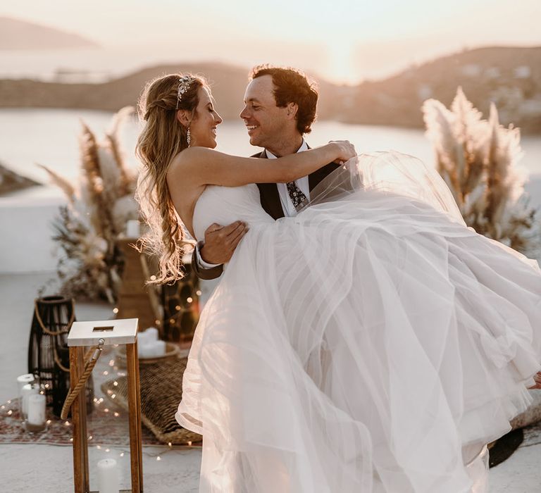 Groom lifts his bride on their wedding day outdoors 