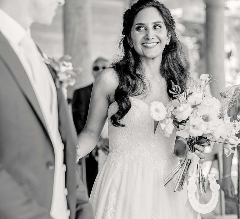 Indian bride wears her black hair in loose curls on her wedding day whilst holding floral bouquet 