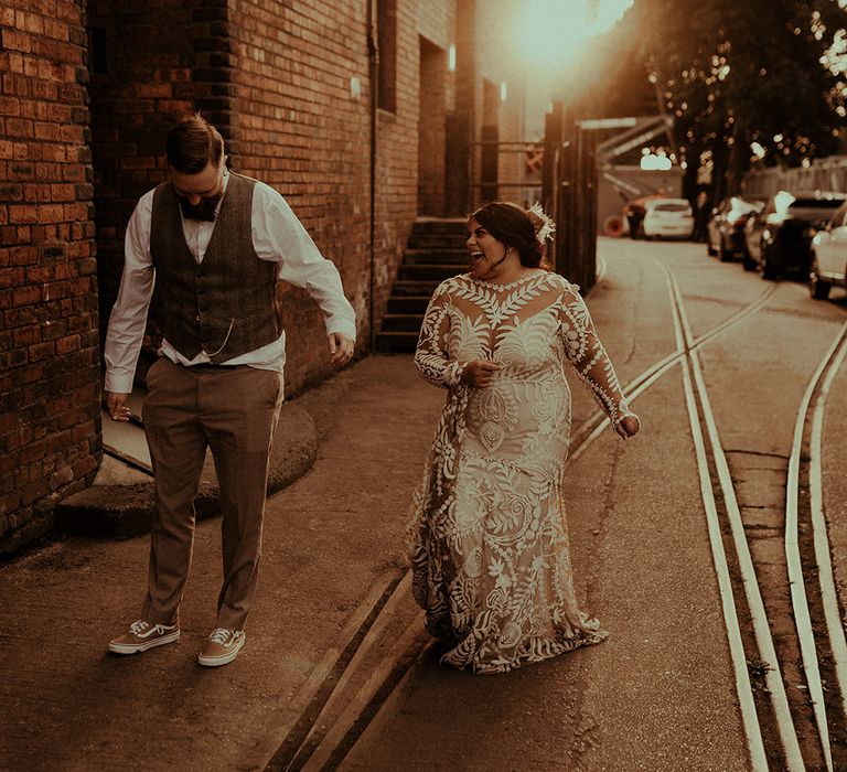 Stylish bride and groom with groom in a tweed waistcoat and trainers and bride in a boho lace wedding dress with long sleeves