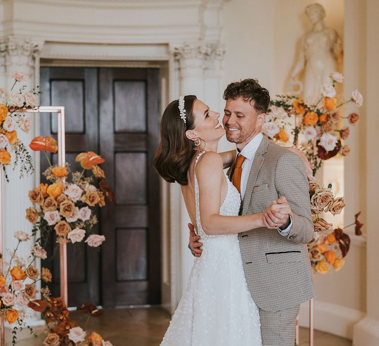 Groom in a beige check suit dancing with his bride in a lace wedding dress at Kirtlington Park wedding venue in Oxfordshire 