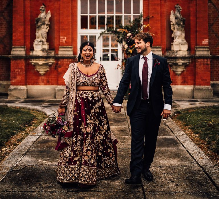 Groom & Bride match in their burgundy wedding outfits and smile at Minley Manor