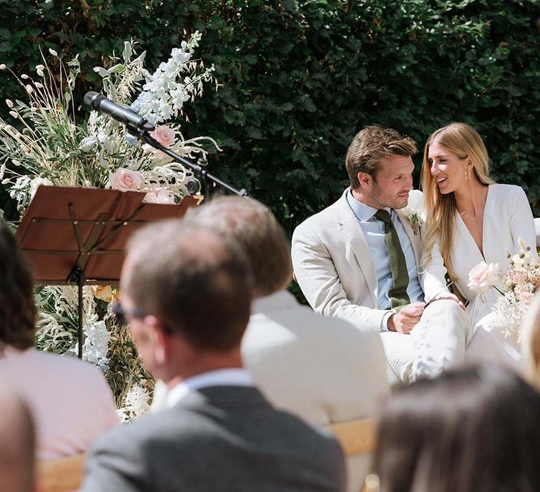 Bride and groom seated at their garden wedding in Bath with stunning pastel summer bouquets