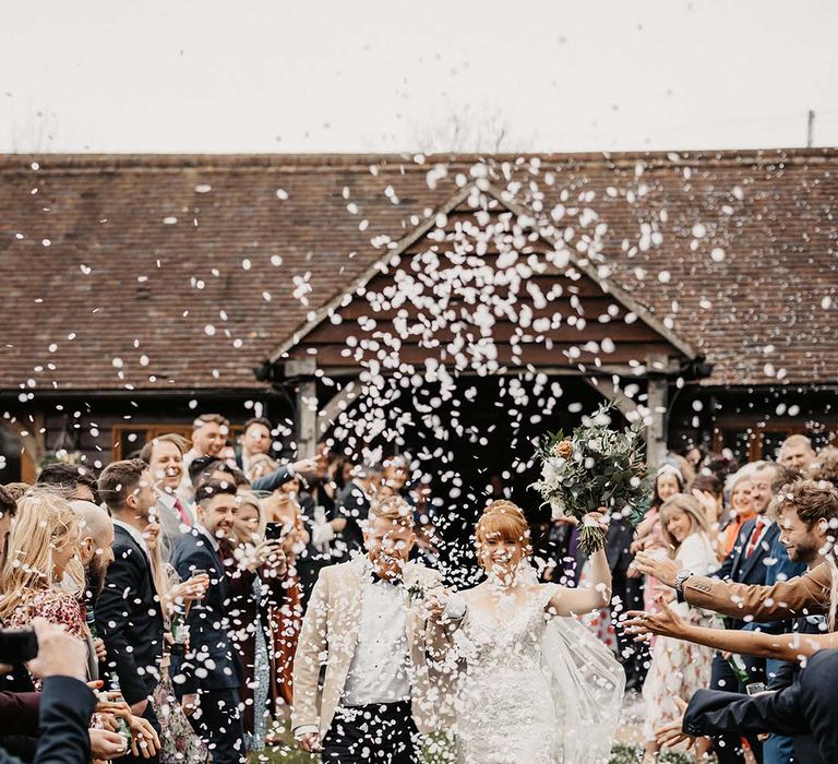 Bride and groom walk through confetti as they eke barn wedding venue on spring day 