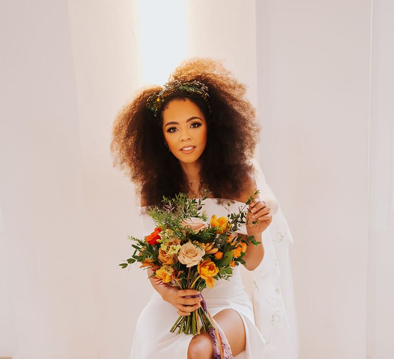 Black bride with afro hair holding a golden wedding bouquet with orange and yellow flowers 