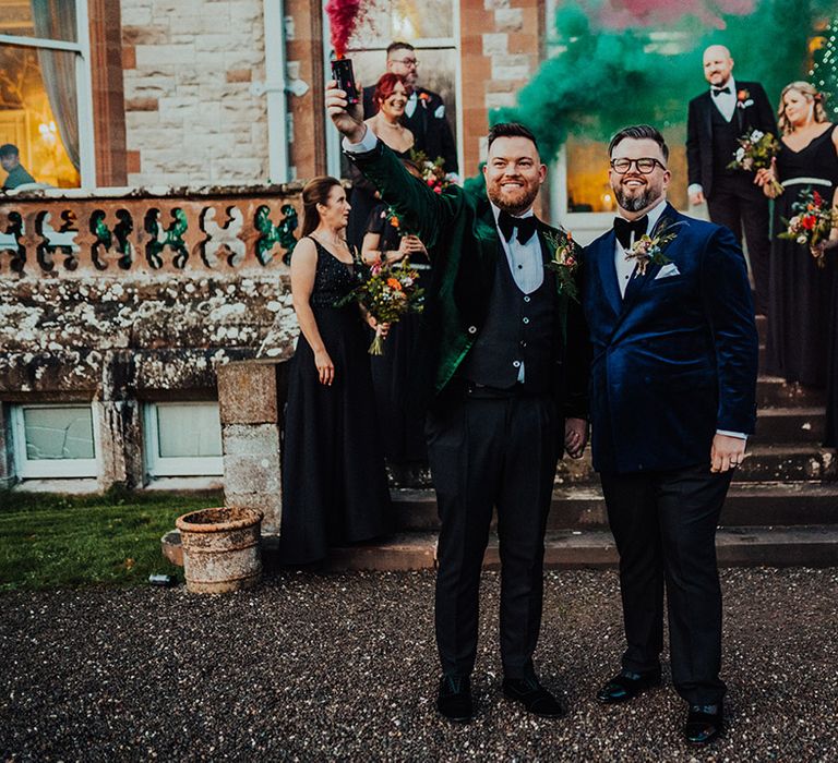 Grooms holding smoke bombs in blue and green suit jackets for LGBTQI+ wedding at Castle Leslie Estate venue