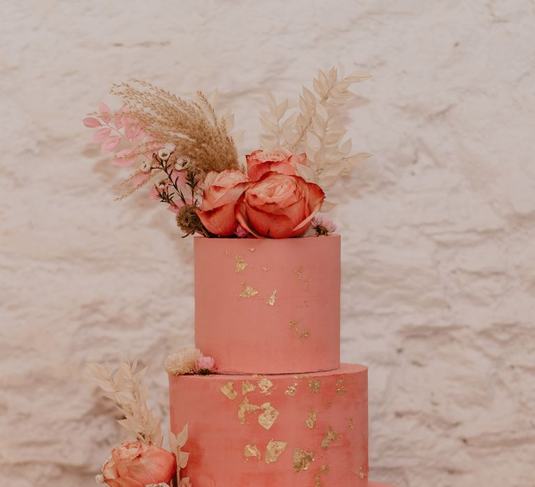 Three tier pink wedding cake with gold flakes complete with roses and dried flower decoration on tree trunk cake stand 