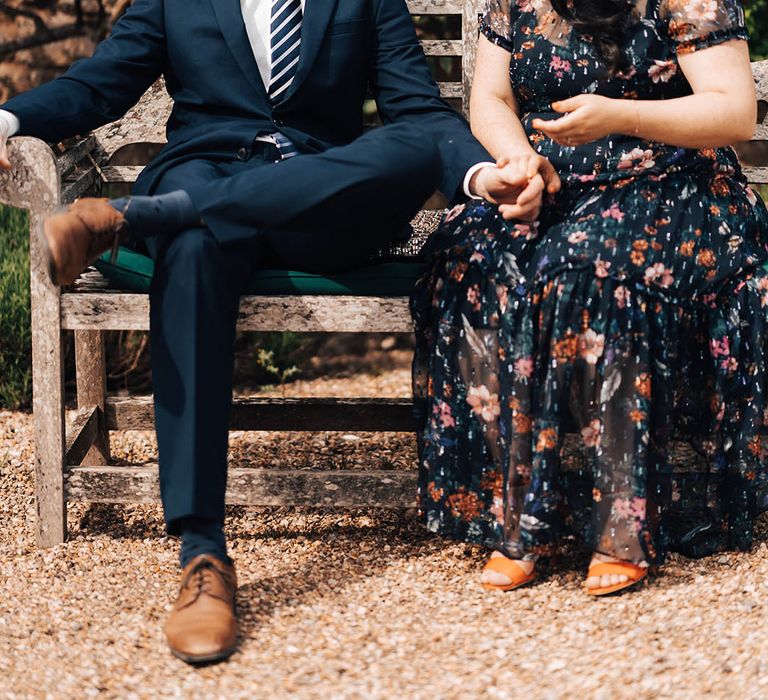 Wedding guests sit together on wooden bench outside Pennard House country house wedding venue