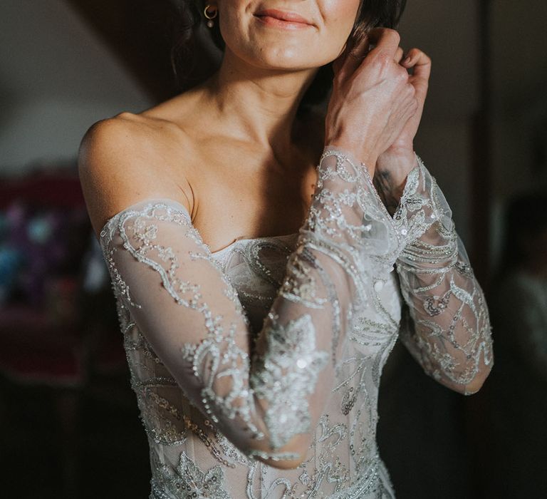 Bride in grey off the shoulder sequinned Zavana Couture wedding dress puts on her earrings