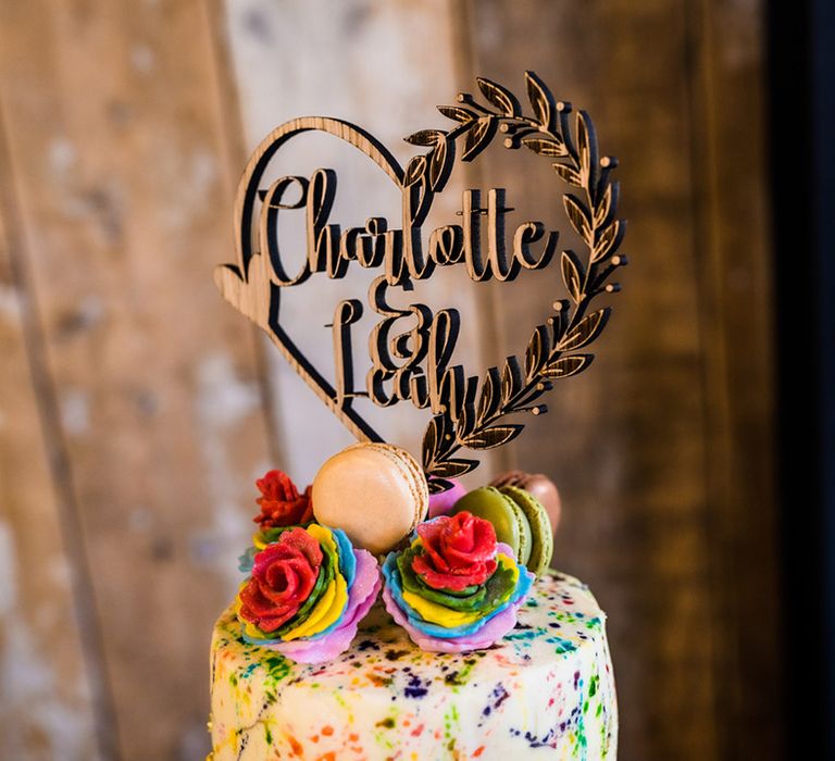 Wooden heart wedding cake topper with the couples' names and rainbow icing roses and macarons