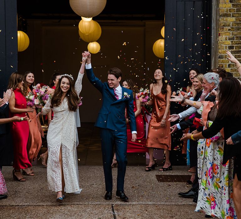 Bride and groom have their confetti exit with bride in lace Rixo dress and groom in blue suit with pink tie