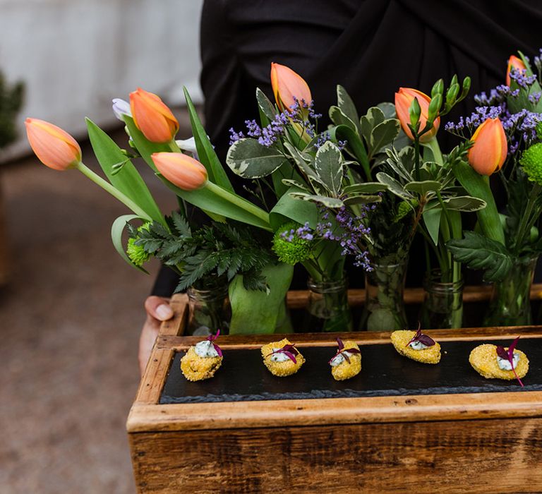 Orange tulips with iris in small vases on a tray for wedding guests