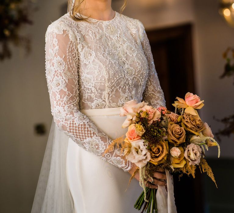 Bride in lace top with long sleeves wedding dress smiling with updo holding autumnal bouquet 