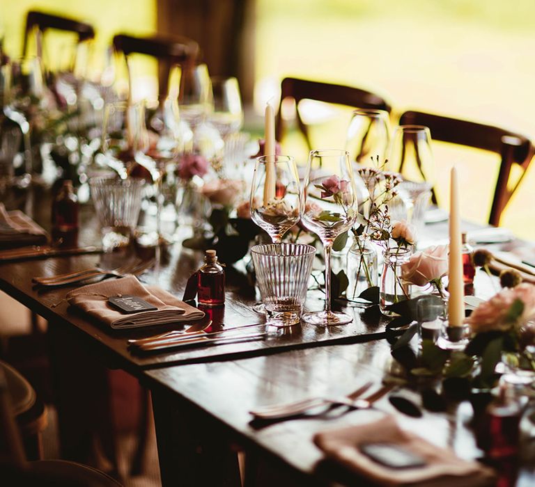 Small pink flower arrangement and white candles with dark wood tables and chairs for reception