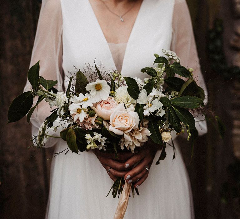 Pink roses, dahlias and white cosmos make up bride's wedding bouquet held by bride 